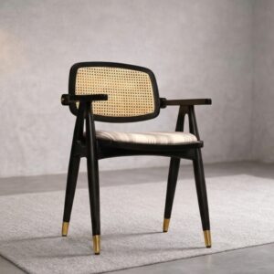 Black wooden dining chair with natural cane mesh backrest, striped upholstered seat, and tapered legs with gold brass tips on a grey rug.
