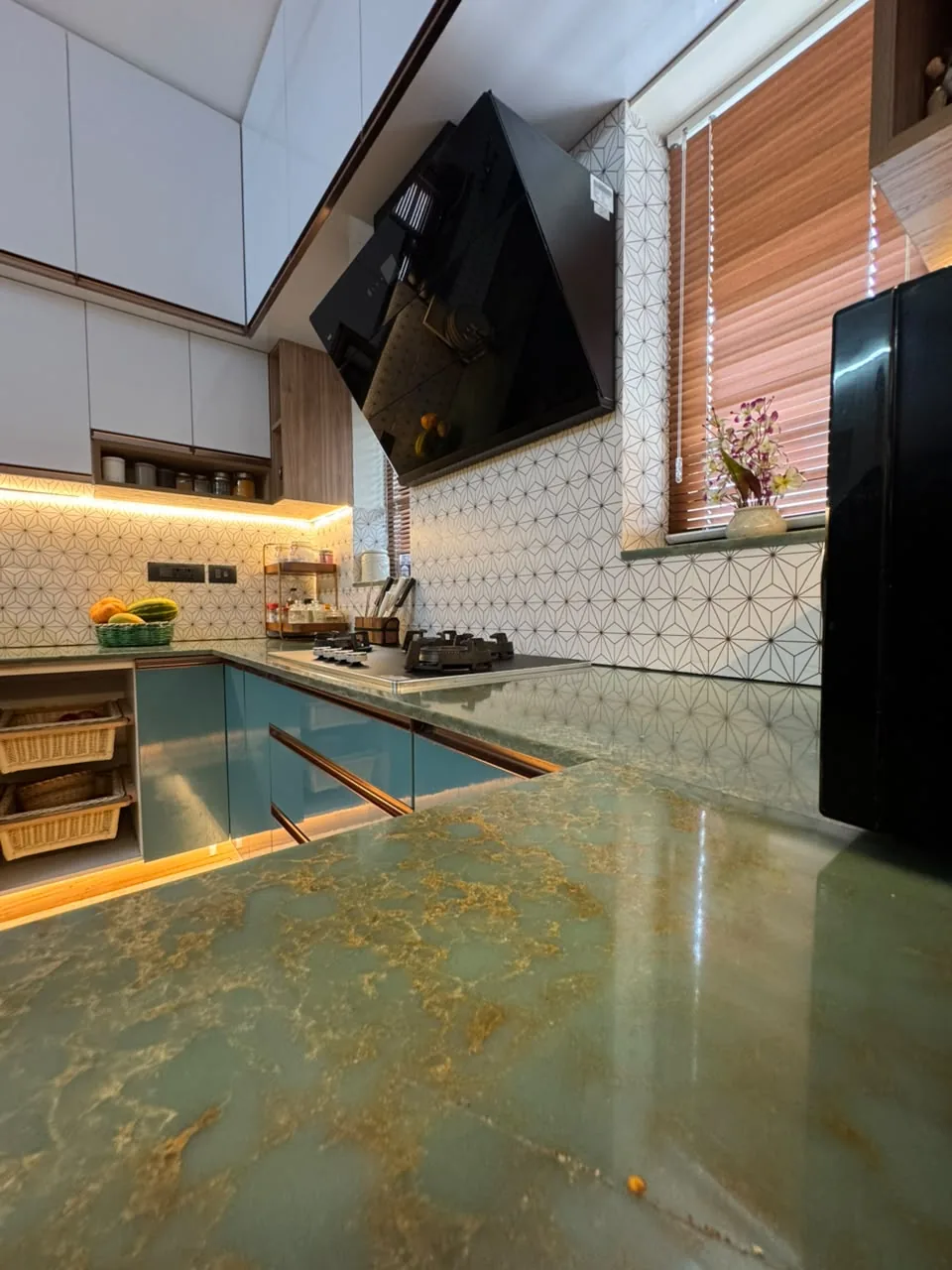 Green and gold natural stone kitchen counter with teal cabinetry and plinth lighting