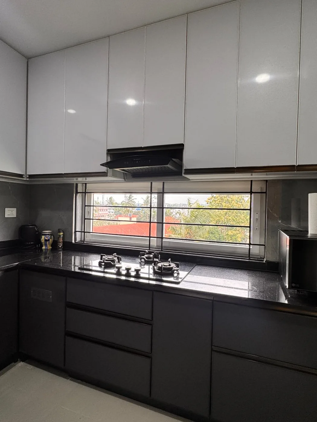 L-shaped modular kitchen in Trivandrum with charcoal gloss base units, white ceiling-height uppers and a black granite counter